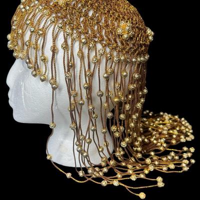 Sale Photo Thumbnail #289: This piece is in the style of a 1920s Flapper headdress. It is gold in color, and features beads throughout. The skull cap is woven. The beaded fringe is intact. Measurement: 16”L. [JP]