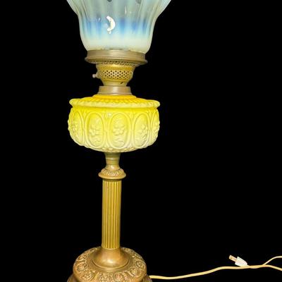 Sale Photo Thumbnail #302: This lamp was electrified at one time. It features an opaque lemon-yellow glass font, and a reeded brass column with a yellowish, opalescent, UV reactive, ruffled glass shade. Measurement: 24”H x 9”W. Pre-auction estimate: $100-$200. [JP]