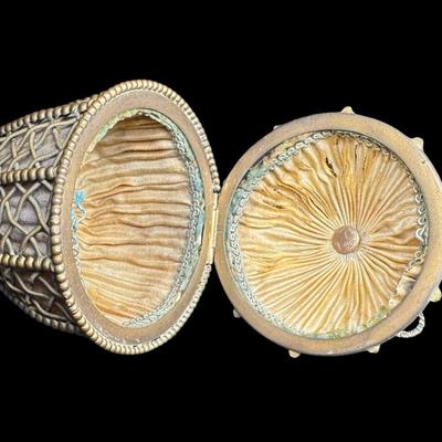 Sale Photo Thumbnail #415: Constructed of brass filigree with a teardrop or egg shaped design. It is hinged with a clasp and findings on either end. The lining inside show wear, although the integrity of the piece is solid. Measurement: 5”H. Pre-auction estimate: $100-$200. [JP]