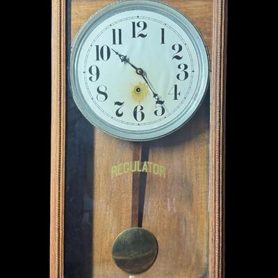 Sale Photo Thumbnail #420: This antique regulator clock has solid oak construction. The integrity of the case and pendulum is solid. There is discoloration in the center of the porcelain face. Not tested. Measurement: 36”H x 18”W. Pre-auction estimate: $100-$150. [RS]