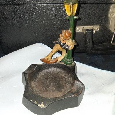 Sale Photo Thumbnail #8: This amazing ashtray features a young gentleman hanging on to the lamp post as he dances in the Rain like Fred Astaire. Good condition with some discoloration to the front as pictured