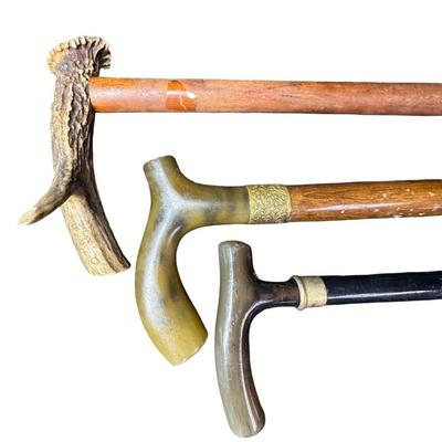 Sale Photo Thumbnail #522: Includes three vintage canes. All three have stag pommels. Two have highly polished pommels, and one is raw antler. They are most likely made of ash wood. Measurement of longest: 39”. [PT]
