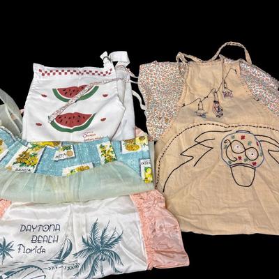 Sale Photo Thumbnail #628: Includes a silk Daytona Beach apron, a floral seed apron, and more. Total of four pieces. There is age related wear, including some stains. [BK]