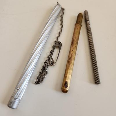 Sale Photo Thumbnail #303: This lot is for a Trio of Vintage Needle Cases.  These nifty little items from the past are needle (or possible pencil lead) holders.  The brass one has a selection of needle within.  The aluminum case has a chain with a safety pin - a very utilitarian pi