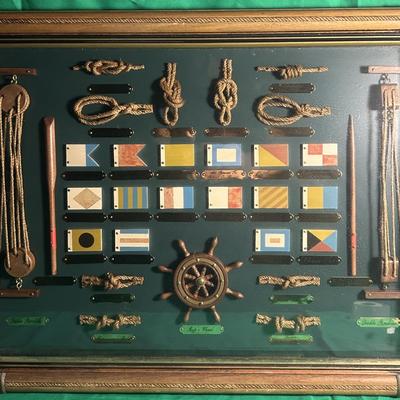 Sale Photo Thumbnail #10: Framed display featuring a collection of nautical items, including a variety of handcrafted knots, signal flags, and a central helm figure. The frame is detailed with a gold border, showcasing mounted examples against a green background. The knots and fla