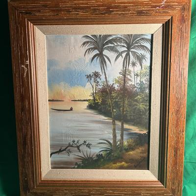 Sale Photo Thumbnail #32: Oil painting depicting a tranquil tropical scene with palm trees, a serene river, and a boat in the distance. The painting is set within a textured wooden frame and is mounted on a fabric mat. No artist signature is visible. The overall frame adds dimensi