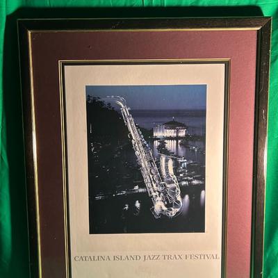 Sale Photo Thumbnail #48: Framed poster from the Catalina Island JazzTrax Festival. Features a nighttime view of Catalina Island with a prominent saxophone superimposed on the scene. Presented in a brown frame with gold accents and includes a matting of complementary tones. Condit