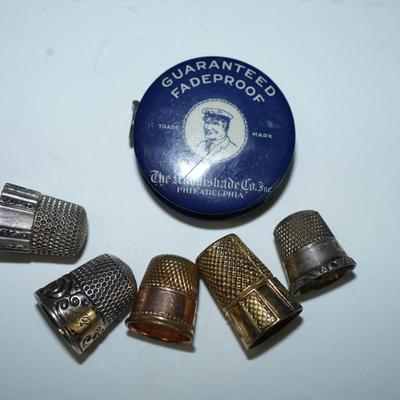 Sale Photo Thumbnail #299: grouping of five thimbles two are stamped sterling, one maybe silverplate, one is rose gold plate and the other is brass, 
vintage tape measure of cloth tape and works good,