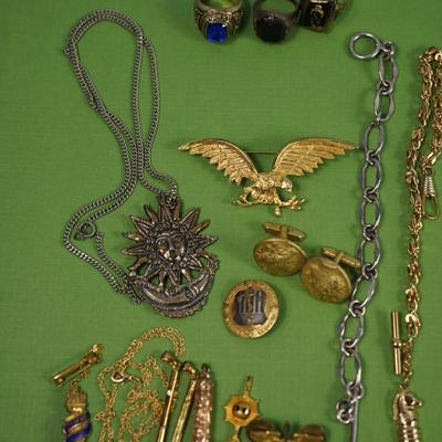 Sale Photo Thumbnail #305: two class rings, onyx and sterling?
white metal and brass watch fobs
eagle pin signed
two avaiator pins -sterling
merchant marine pin - sterling'
brass cuff link of roman coin repro 
rose gold plate golf or card pencil
Alva sun burst pendant 
other...