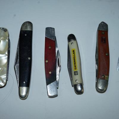 Sale Photo Thumbnail #312: grouping of six pocket knives. two wood and other. Mother of pearl style finish plastic 

Caterpillar advertising ( good condition) hardplastic case decal 
there are stains on the wood  handled knives and the 1" one is not working -lever to fold into the 