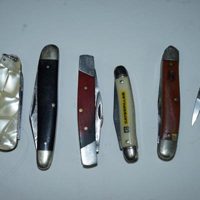 Sale Photo Thumbnail #311: grouping of six pocket knives. two wood and other. Mother of pearl style finish plastic 

Caterpillar advertising ( good condition) hardplastic case decal 
there are stains on the wood  handled knives and the 1" one is not working -lever to fold into the 