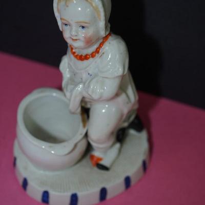 Sale Photo Thumbnail #363: Circa 1910 glazed porcelain match keep, the base of the figurine is a stike for the match, 
Little novelty of a baby about to sit on the commode. Its doll behind him. 
Height 5" 
the base measiures 4" by 3 1/4"
Good condition, slight wear to the base. and