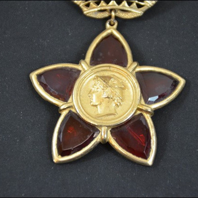 art deco pin, award of mercury surrounded by a red five petal flower with a crow