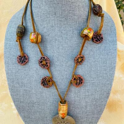 AA   GROOVY HIPPY PENDANT OF CLAY W/CERAMIC BEADS & WALNUT SLICES STRUNG ON LEATHER.