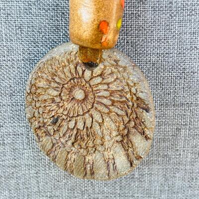 AA   GROOVY HIPPY PENDANT OF CLAY W/CERAMIC BEADS & WALNUT SLICES STRUNG ON LEATHER.