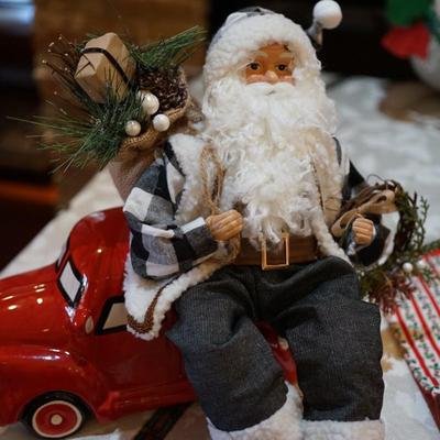 HOLIDAY GROUPING. HAND CRAFTED SANTA IN FLANNEL SHIRT CARRYING BOUGHS OF GREENS AND GIFTS SITS ON CERAMIC RED TRUCK / THREE HAND CRAFTED...