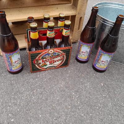 Wooden crate with Metal handled oval Ice tub, tall Fat tire beer bottles and Christmas brew 6 pack bottles.
