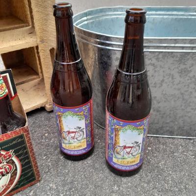 Wooden crate with Metal handled oval Ice tub, tall Fat tire beer bottles and Christmas brew 6 pack bottles.