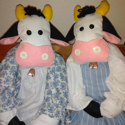 Two crafted cow dolls and a pig doll on a wooden bench