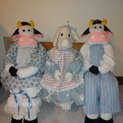 Two crafted cow dolls and a pig doll on a wooden bench