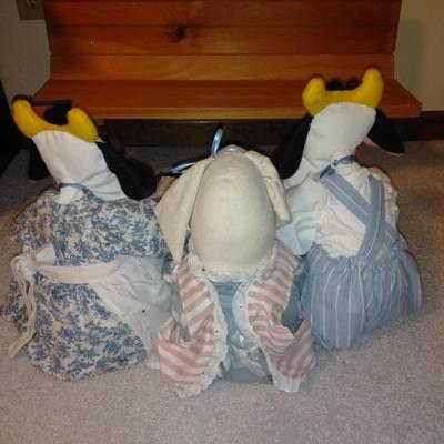 Two crafted cow dolls and a pig doll on a wooden bench