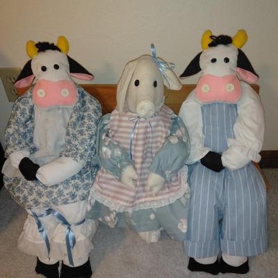 Two crafted cow dolls and a pig doll on a wooden bench
