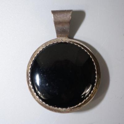 NAVAJO SILVER WORKED PENDANT OF RUG WEAVER ON ONE SIDE BLACK ONYX DISC ON OTHER.