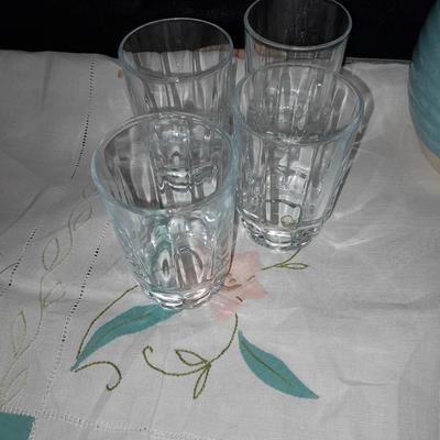 Blue pitcher with bee, coffee mug, metal rooster decor, and glasses with embroidered linen table runner