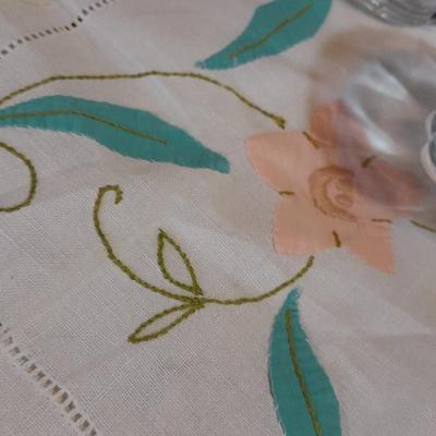 Blue pitcher with bee, coffee mug, metal rooster decor, and glasses with embroidered linen table runner