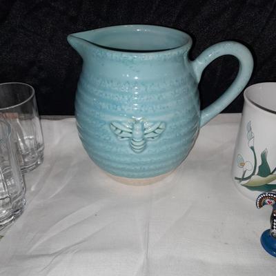 Blue pitcher with bee, coffee mug, metal rooster decor, and glasses with embroidered linen table runner