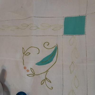 Blue pitcher with bee, coffee mug, metal rooster decor, and glasses with embroidered linen table runner