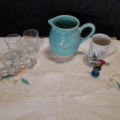 Blue pitcher with bee, coffee mug, metal rooster decor, and glasses with embroidered linen table runner