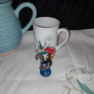 Blue pitcher with bee, coffee mug, metal rooster decor, and glasses with embroidered linen table runner