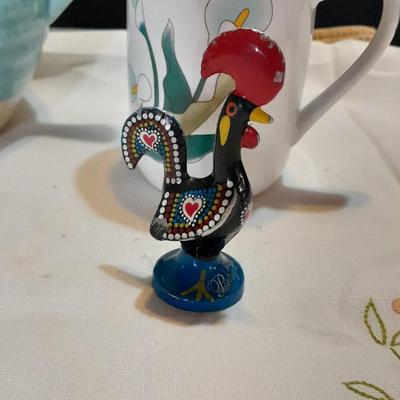 Blue pitcher with bee, coffee mug, metal rooster decor, and glasses with embroidered linen table runner