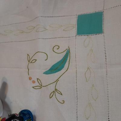 Blue pitcher with bee, coffee mug, metal rooster decor, and glasses with embroidered linen table runner