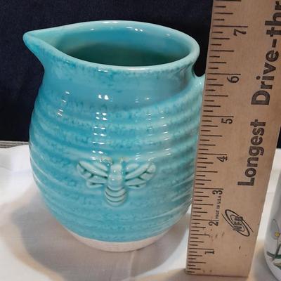 Blue pitcher with bee, coffee mug, metal rooster decor, and glasses with embroidered linen table runner