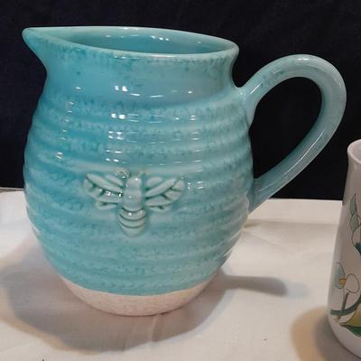 Blue pitcher with bee, coffee mug, metal rooster decor, and glasses with embroidered linen table runner