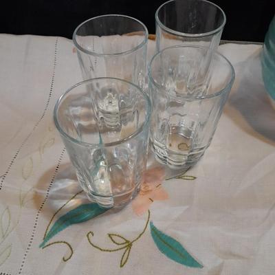 Blue pitcher with bee, coffee mug, metal rooster decor, and glasses with embroidered linen table runner