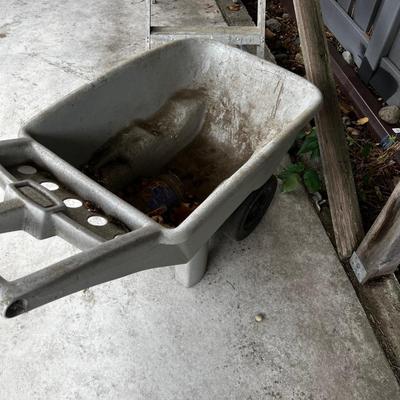 Behind GARAGE -- Plastic wheel barrow