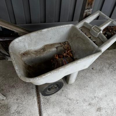 Behind GARAGE -- Plastic wheel barrow