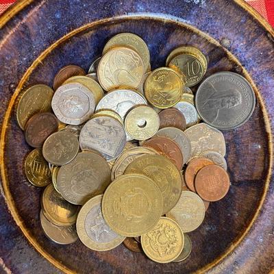 Assorted foreign coins in blue ceramic bowl.