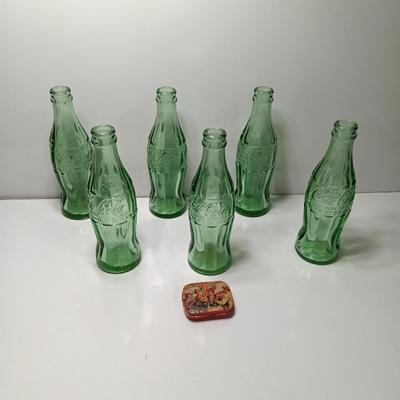 Six glass Coca Cola bottles and small coca cola collectible tin