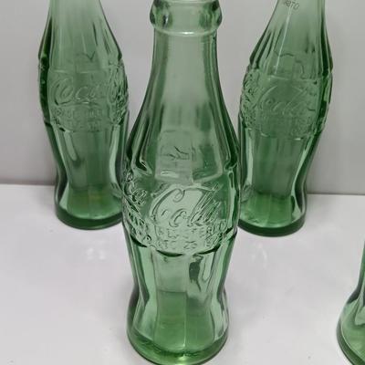 Six glass Coca Cola bottles and small coca cola collectible tin