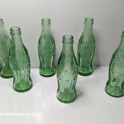 Six glass Coca Cola bottles and small coca cola collectible tin