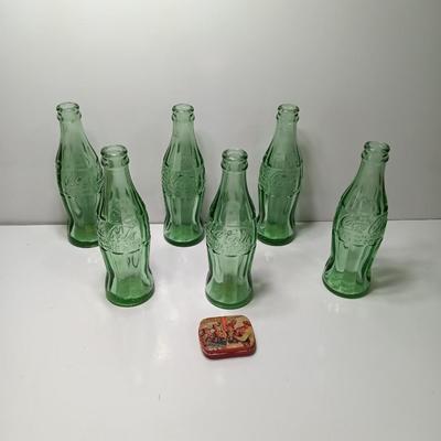Six glass Coca Cola bottles and small coca cola collectible tin