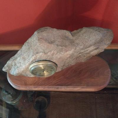 A CLOCK MOUNTED INTO A ROCK AND FIXED ONTO A WOODEN BASE