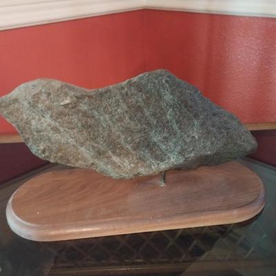 A CLOCK MOUNTED INTO A ROCK AND FIXED ONTO A WOODEN BASE