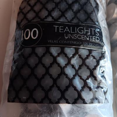 Two unopened bags of 100 ea. unscented tea light candles and a decorative pillar candle