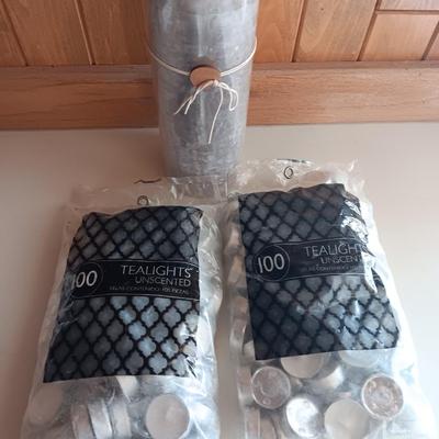 Two unopened bags of 100 ea. unscented tea light candles and a decorative pillar candle