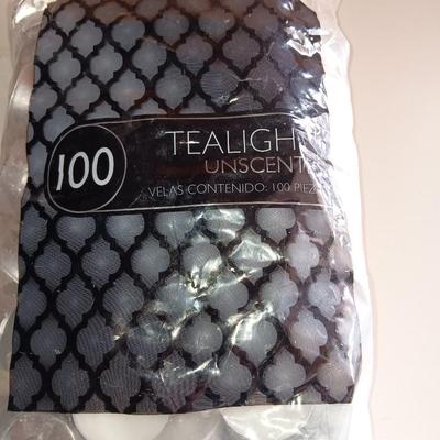 Two unopened bags of 100 ea. unscented tea light candles and a decorative pillar candle